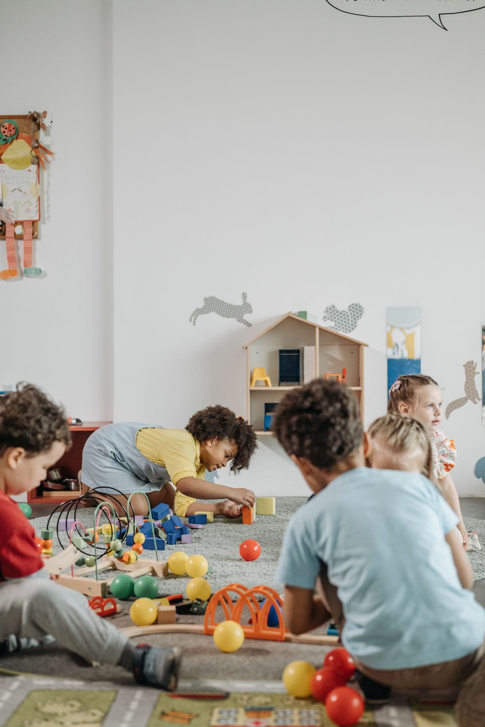 De jeunes enfants, surtout vus de dos, qui jouent avec des jouets sur le sol d'une salle de jeux de garderie