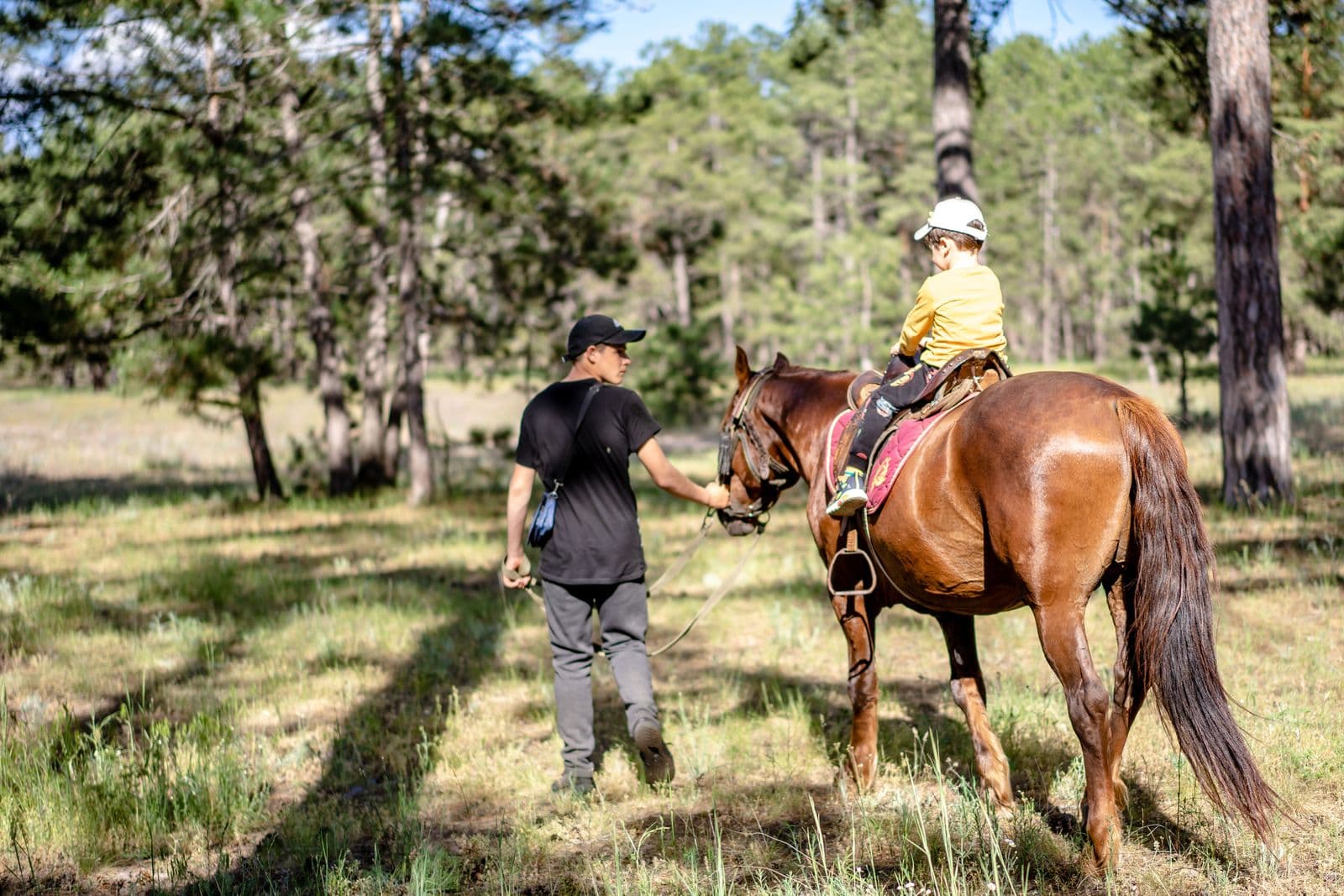 Un enfant casqué sur un cheval mené par un moniteur le long d'un sentier en forêt