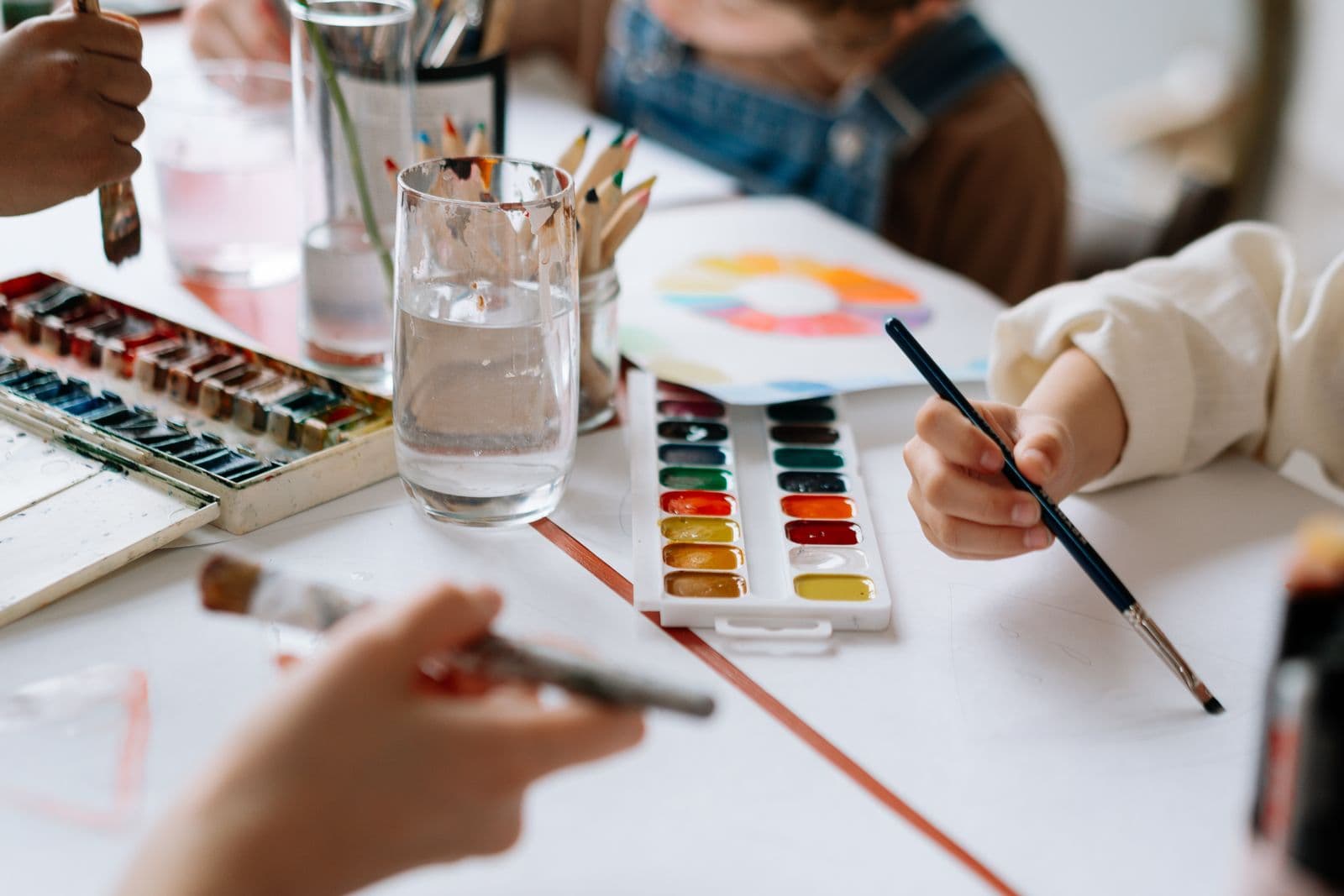 Des mains d'enfants qui peignent à l'aquarelle sur une table de cours