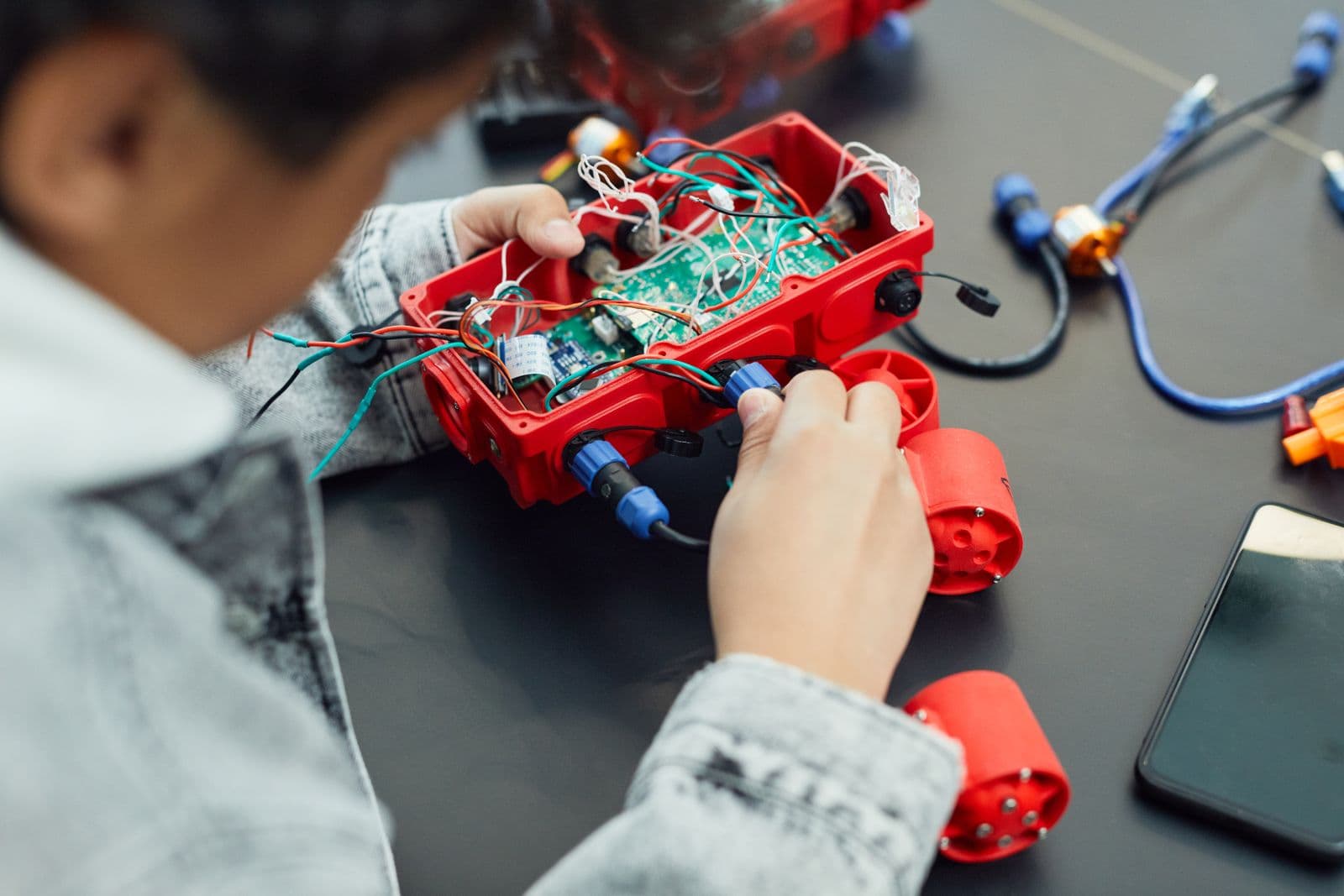 Les mains d'un enfant qui câble un petit robot sur une table de classe
