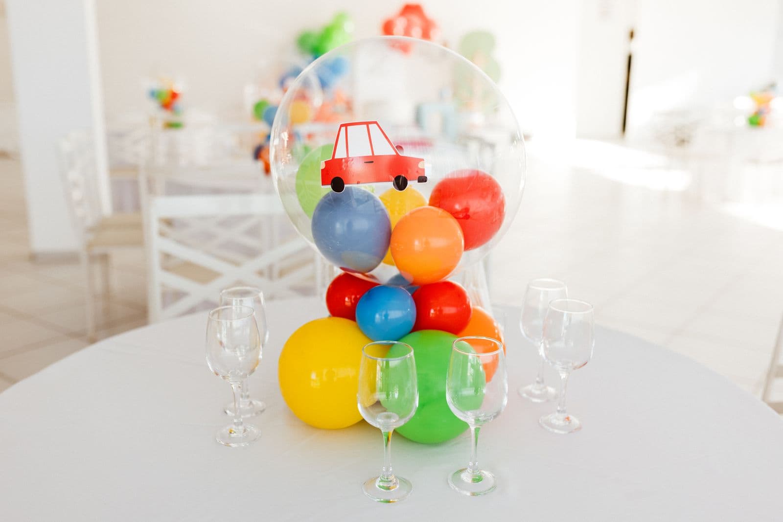 Un centre de table en ballons colorés et des verres sur une table de fête blanche