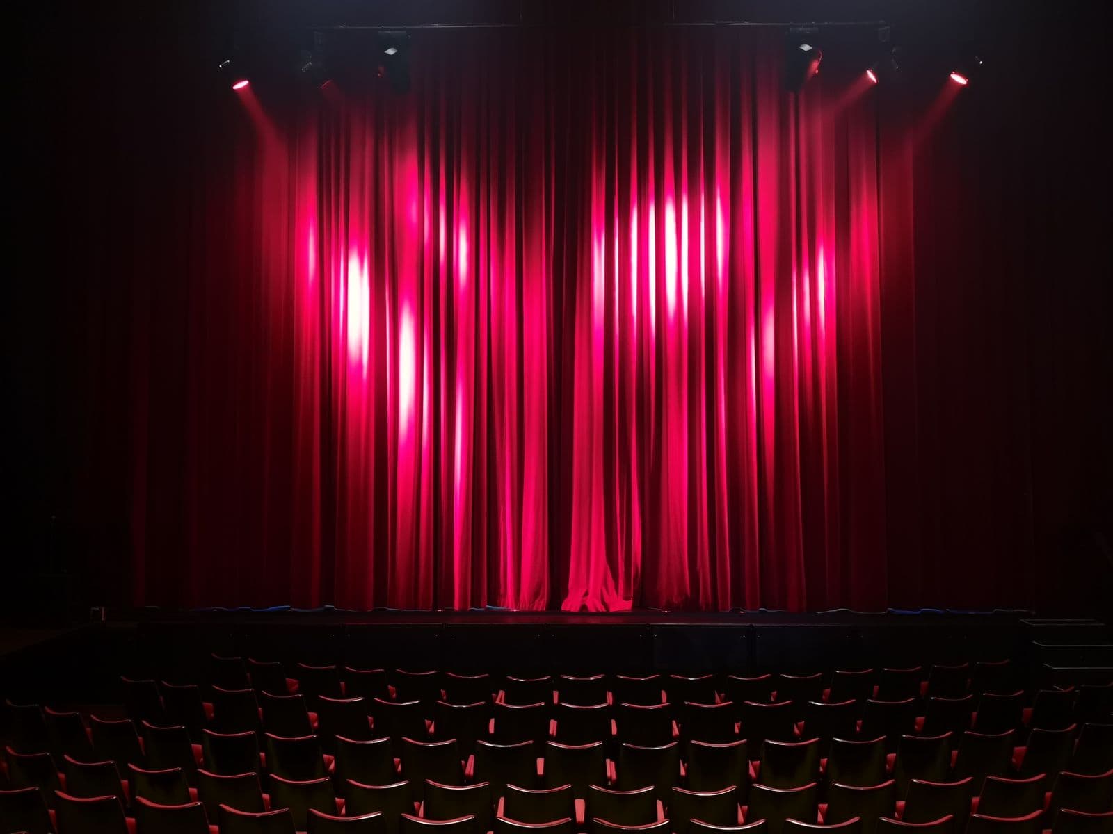 Une scène de théâtre vide aux rideaux rouges sous les projecteurs, vue depuis les sièges