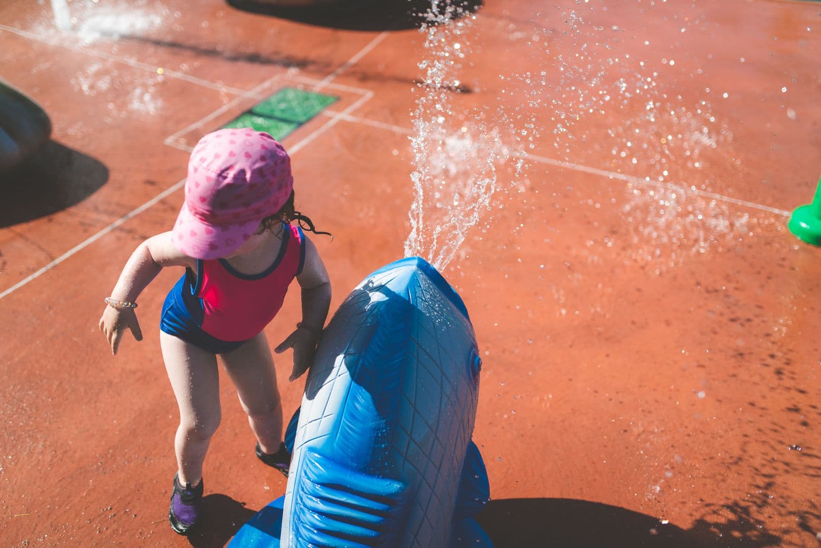 Un tout-petit portant un chapeau de soleil qui joue près d'un jet d'eau