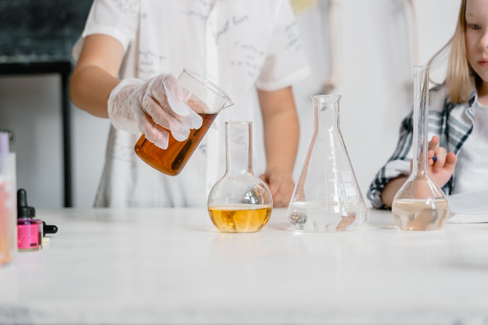 Des mains d'enfants qui versent un liquide coloré d'un flacon à l'autre pendant un cours de sciences