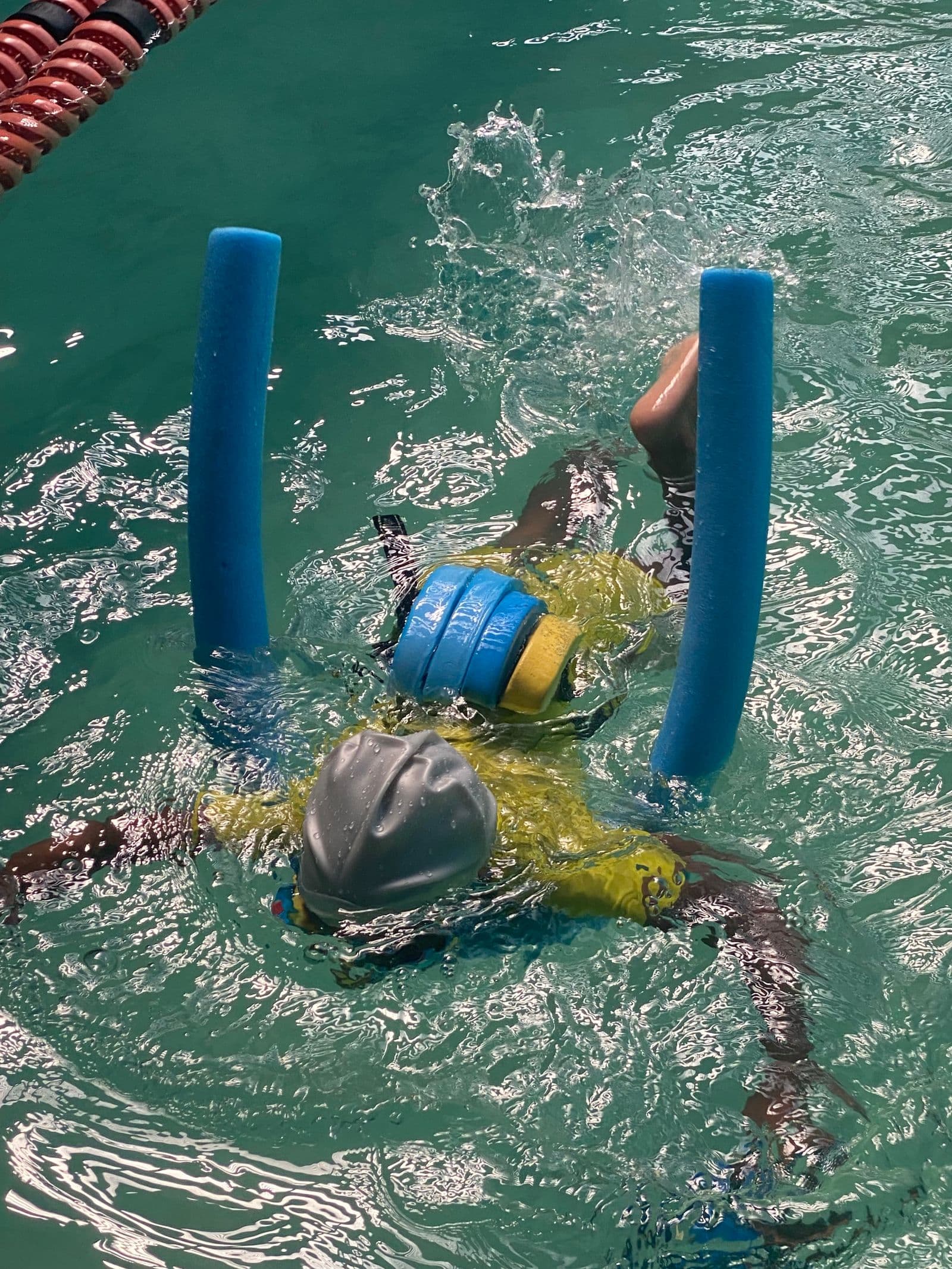 Un enfant avec un bonnet de bain et une ceinture de flottaison, la tête dans l'eau, qui apprend à nager avec des frites